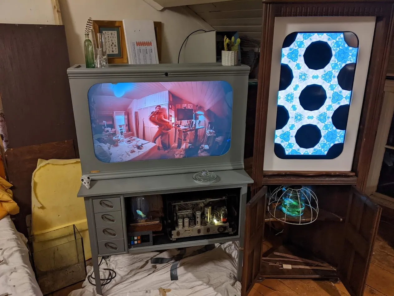 Two screens with in a grey cabinet and a tall corner cabinet.