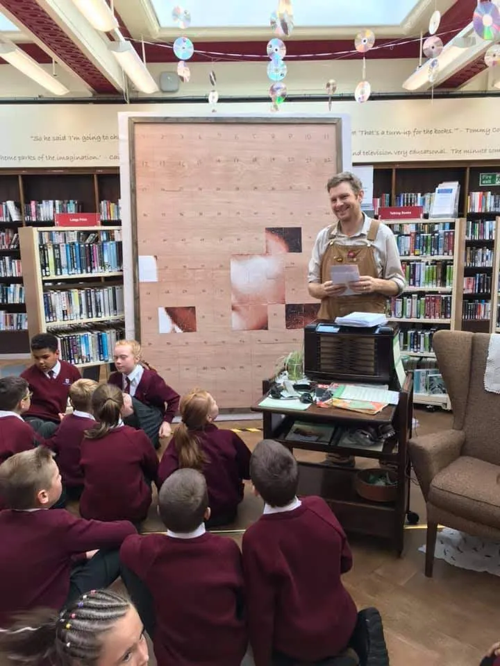 Man standing in front of primary school children in library.