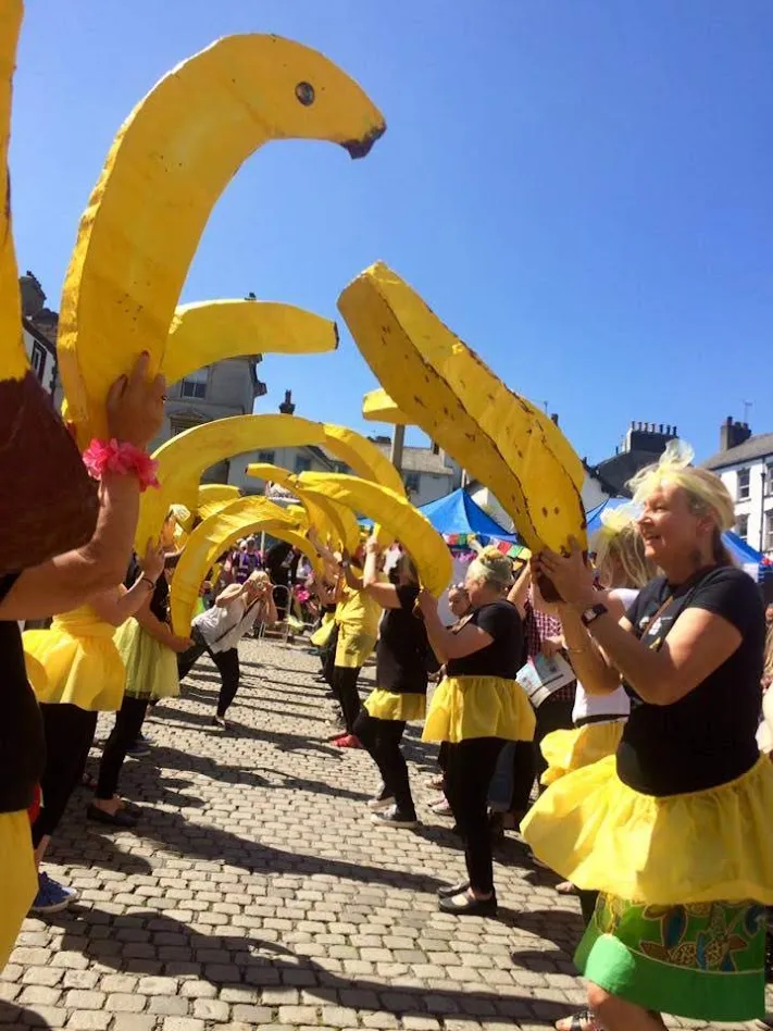 Two lines of people face each other holding bananas aloft.