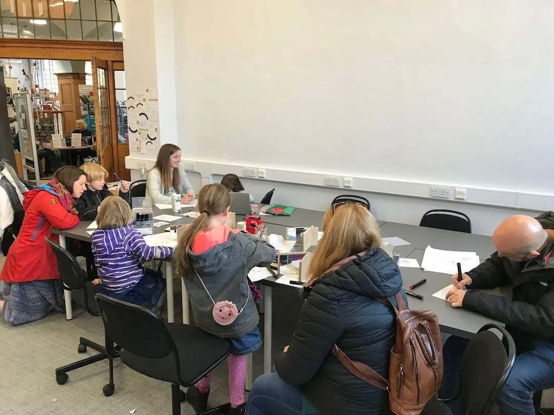 Children and grown-ups sitting and kneeling around a table drawing on sheets of paper.