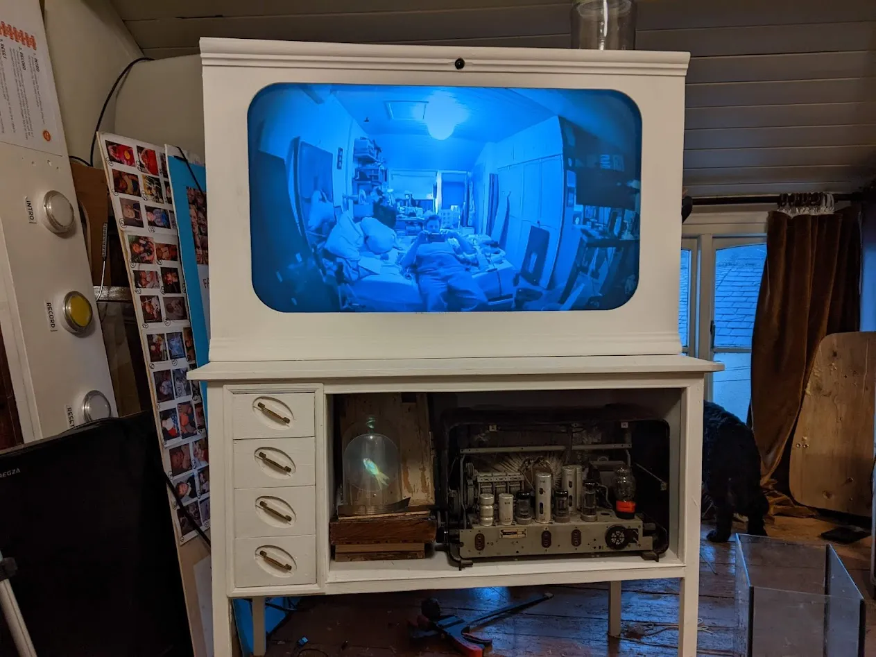 White cabinet with TV screen with floating goldfish in bell jar below.
