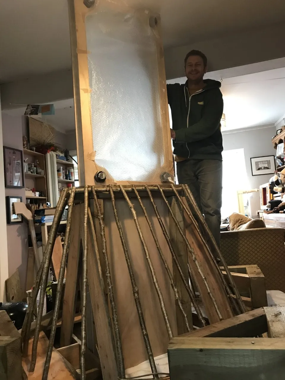Man standing next to wooden poles attached in a pyramid shape