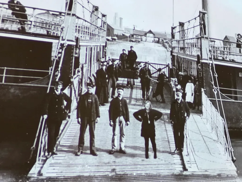 a ferry with 5 people standing on the ramp looking at the camera.