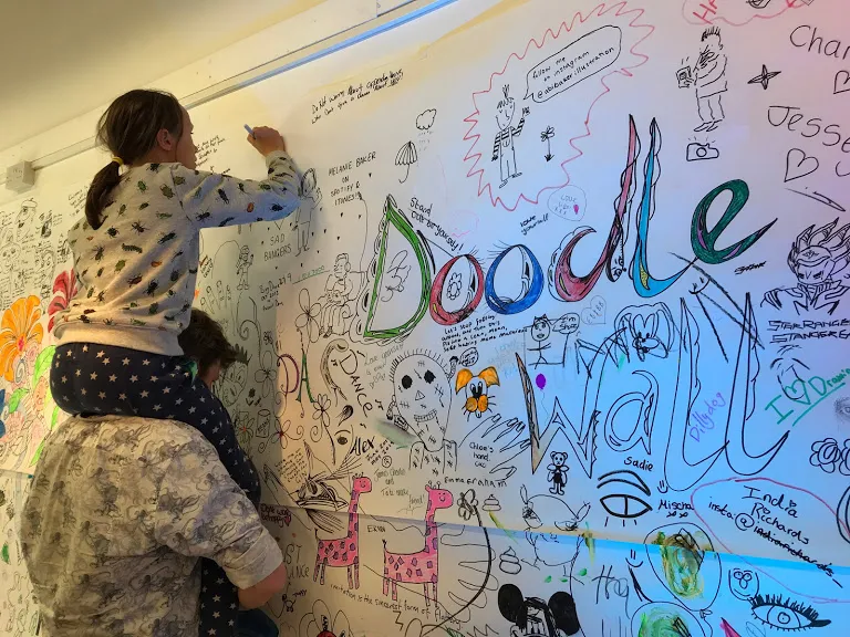 Girl on father's shoulders drawing on wall.