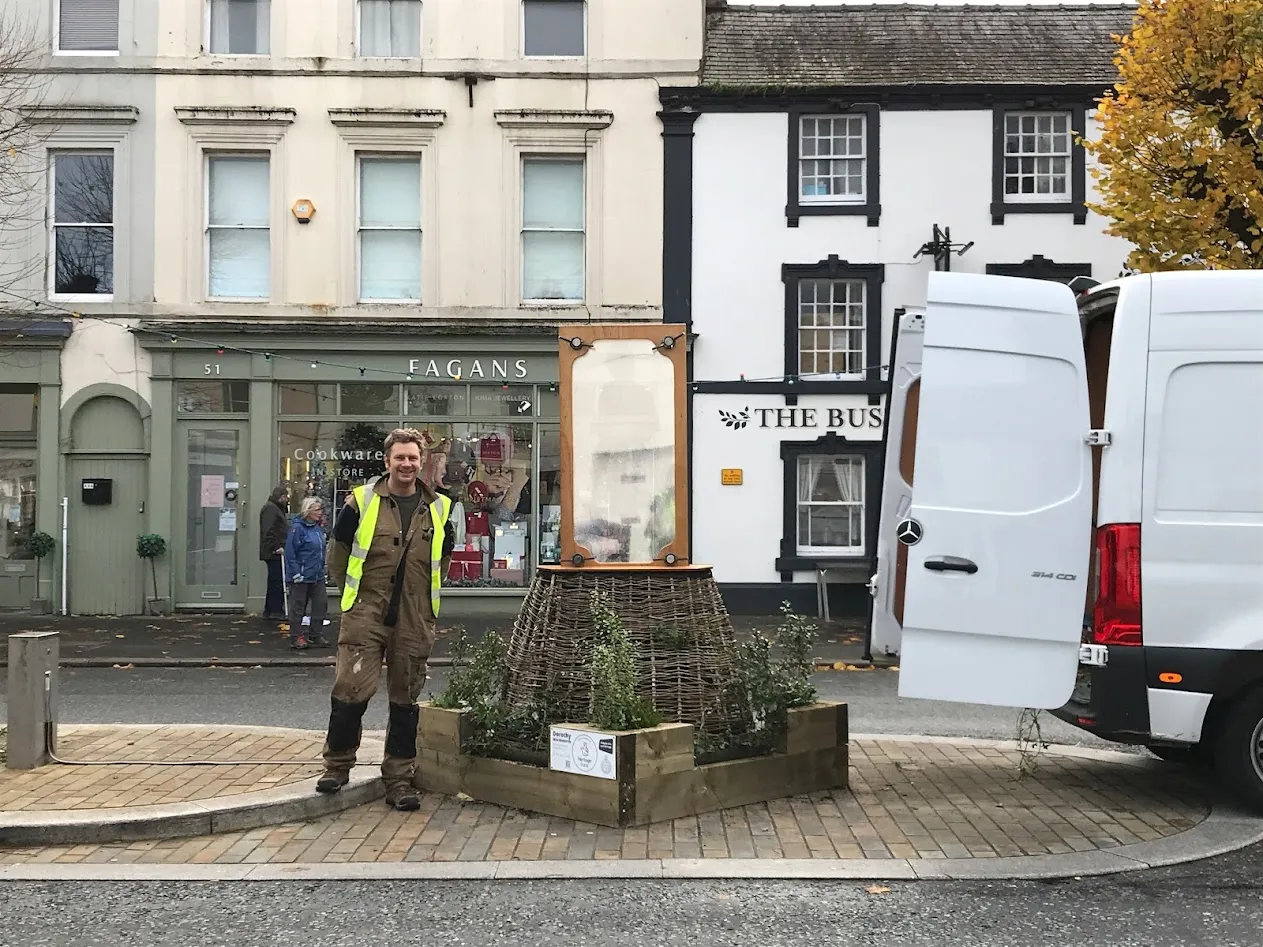 Man leaning on a wooden structure next to a van and large statue.