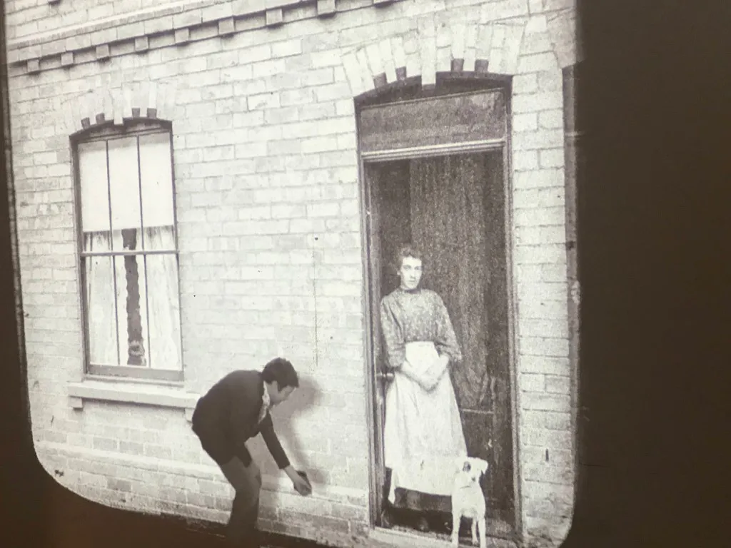 woman standing in her doorway with a dog. Man bending down to feed the dog.