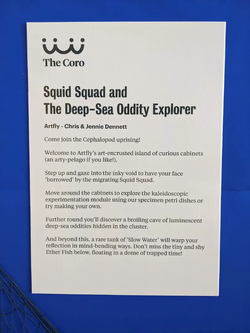 Art panel saying: Squid Squad and The Deep-Sea Oddity Explorer Artfly - Chris & Jennie Dennett Come join the Cephalopod uprising! Welcome to Artfly's art-encrusted island of curious cabinets (an arty-pelago if you like!). Step up and gaze into the inky void to have 'borrowed' by the migrating Squid Squad. your face Move around the cabinets to explore the kaleidoscopic experimentation module using our specimen petri dishes or try making your own. Further round you'll discover a broiling cave of luminescent deep-sea oddities hidden in the cluster. And beyond this, a rare tank of 'Slow Water' will warp your reflection in mind-bending ways. Don't miss the tiny and shy Ether Fish below, floating in a dome of trapped time!