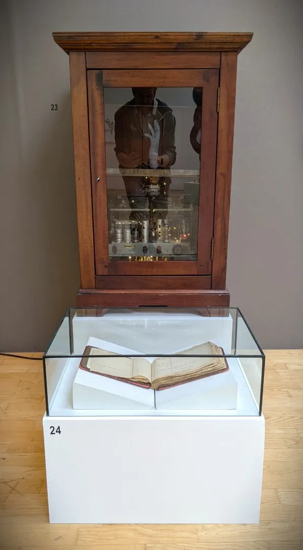 Cabinet behind a short white block holding an open book against an brown wall.