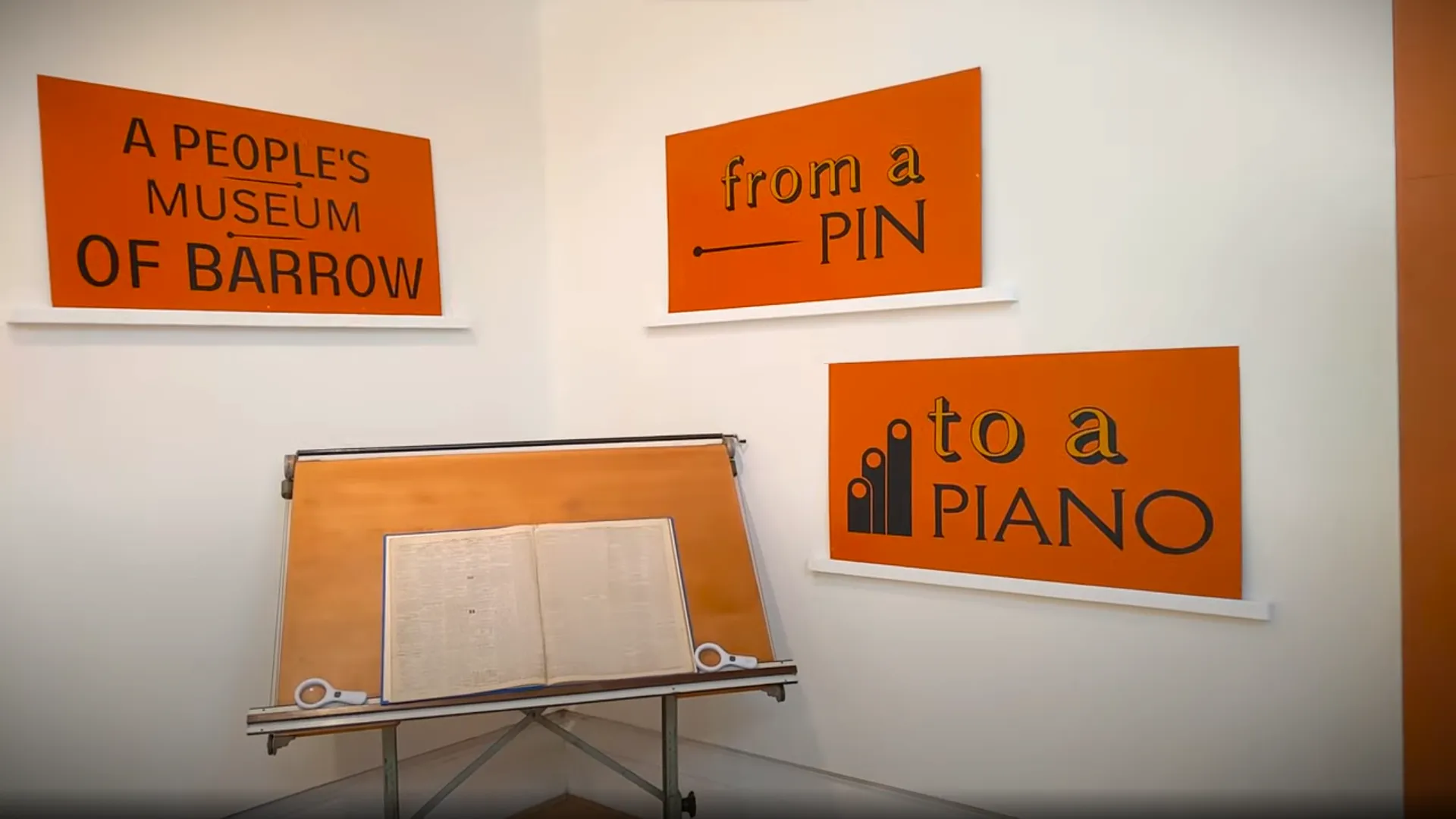 Cabinet behind a short white block holding an open book against an brown wall.