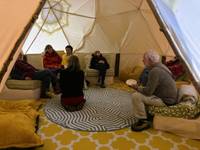 People sitting and kneeling in a circle inside a tent.