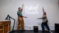 Two people in front of a white wall holding arms to frame logo saying Full of Noises.